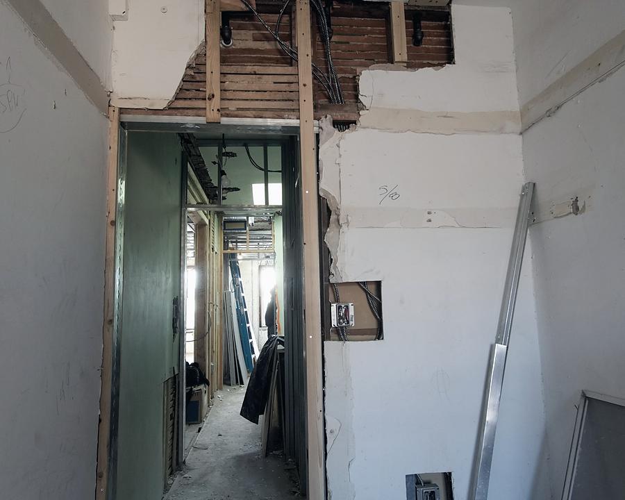 A stripped corridor before work — open ceiling, exposed joists, bare walls