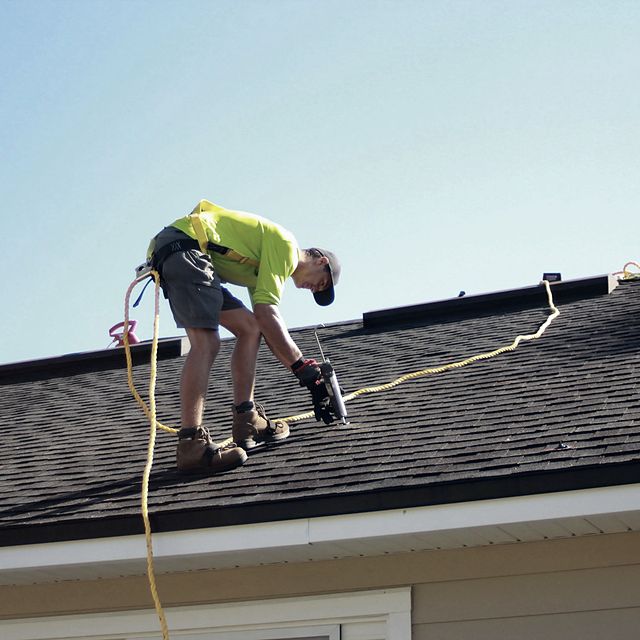 Roofer fastening shingles on a residential roof