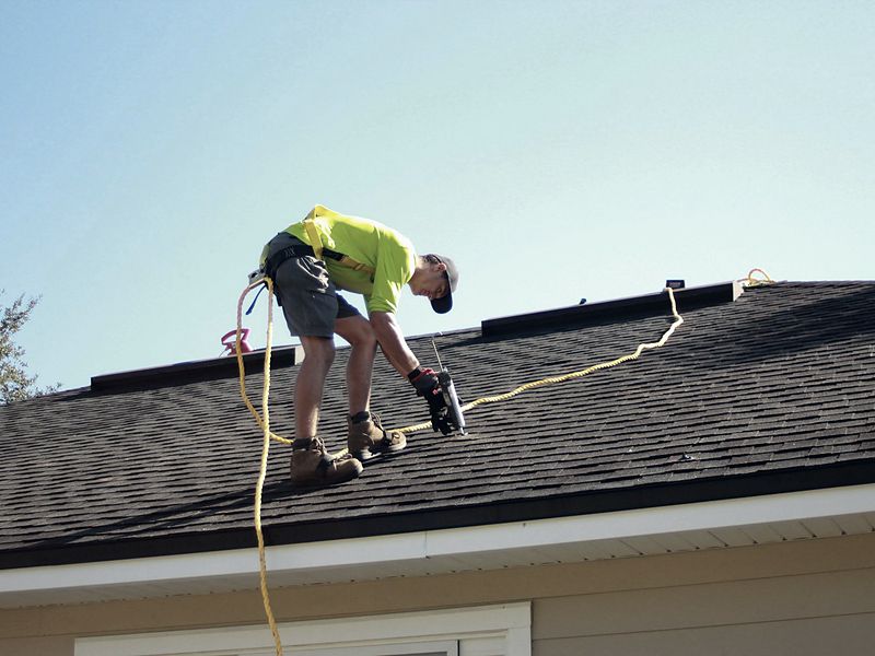 Roofer fastening shingles on a residential roof
